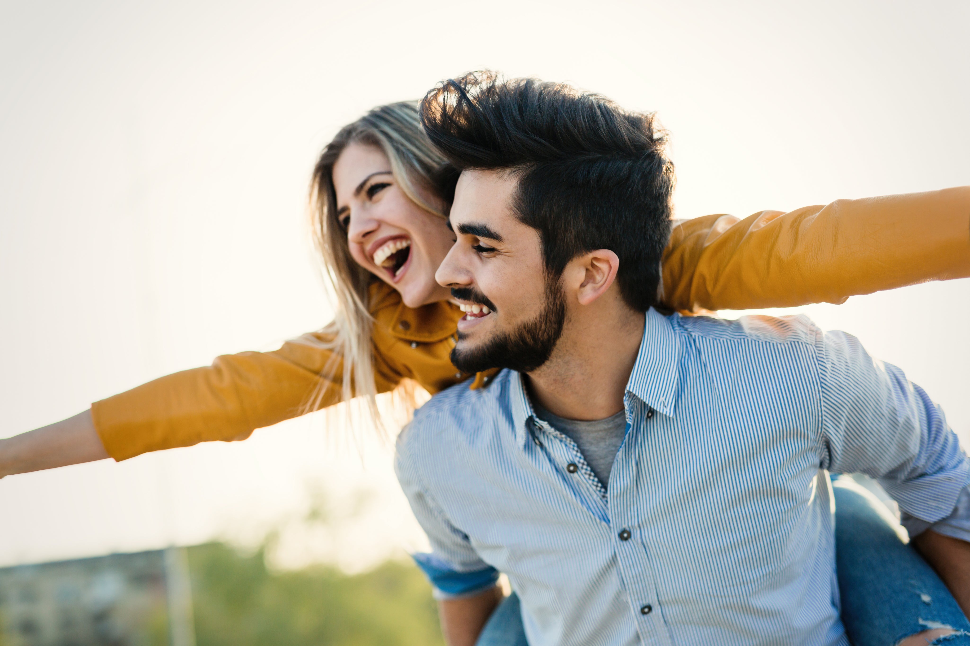 Man and woman laughing together outdoors with a clear sky background